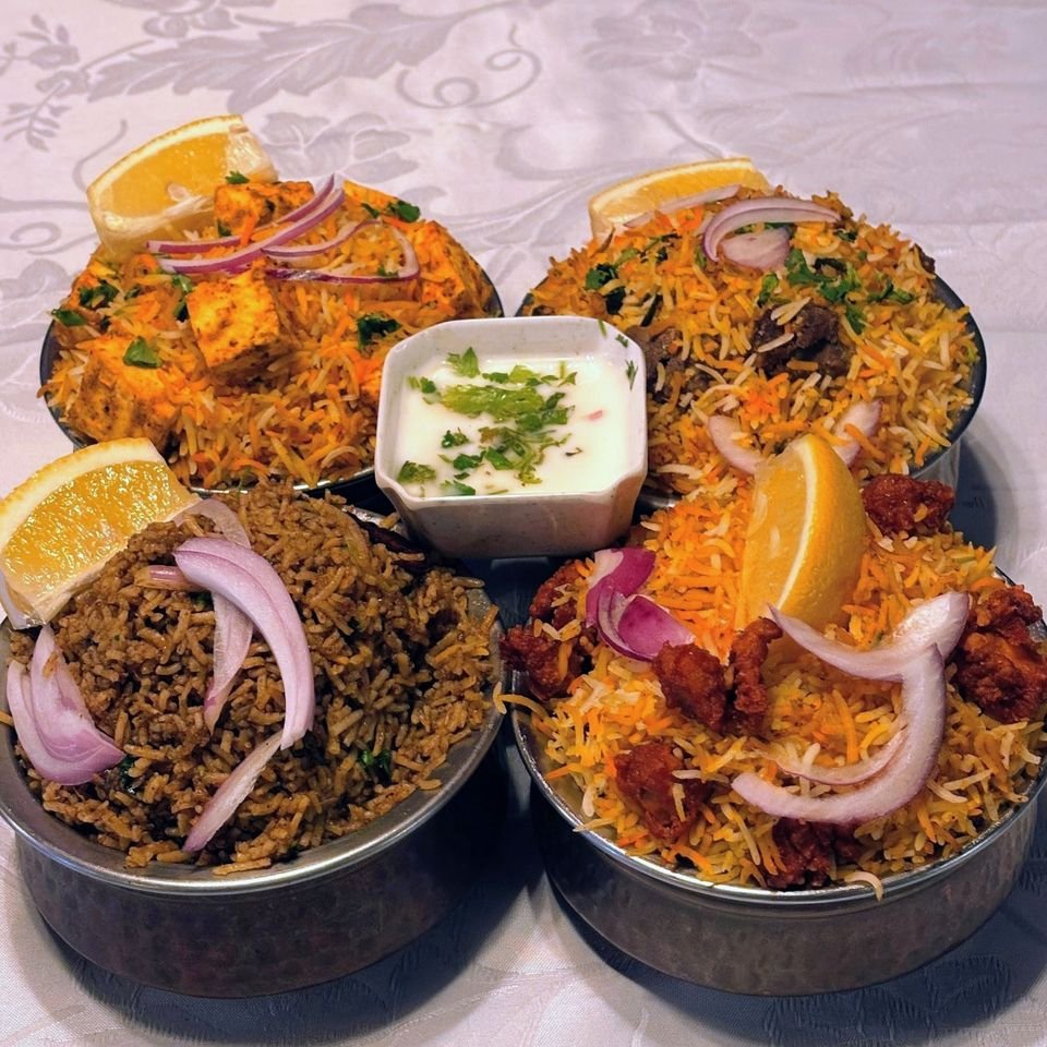 Four dum biryanis in steel handis with raita and lemon