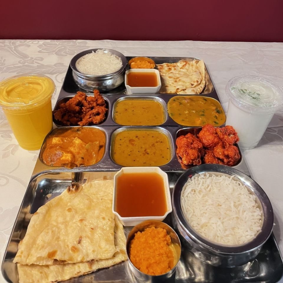 Lunch thali tray with dal, curries, rice, naan, raita, halwa and mango lassi